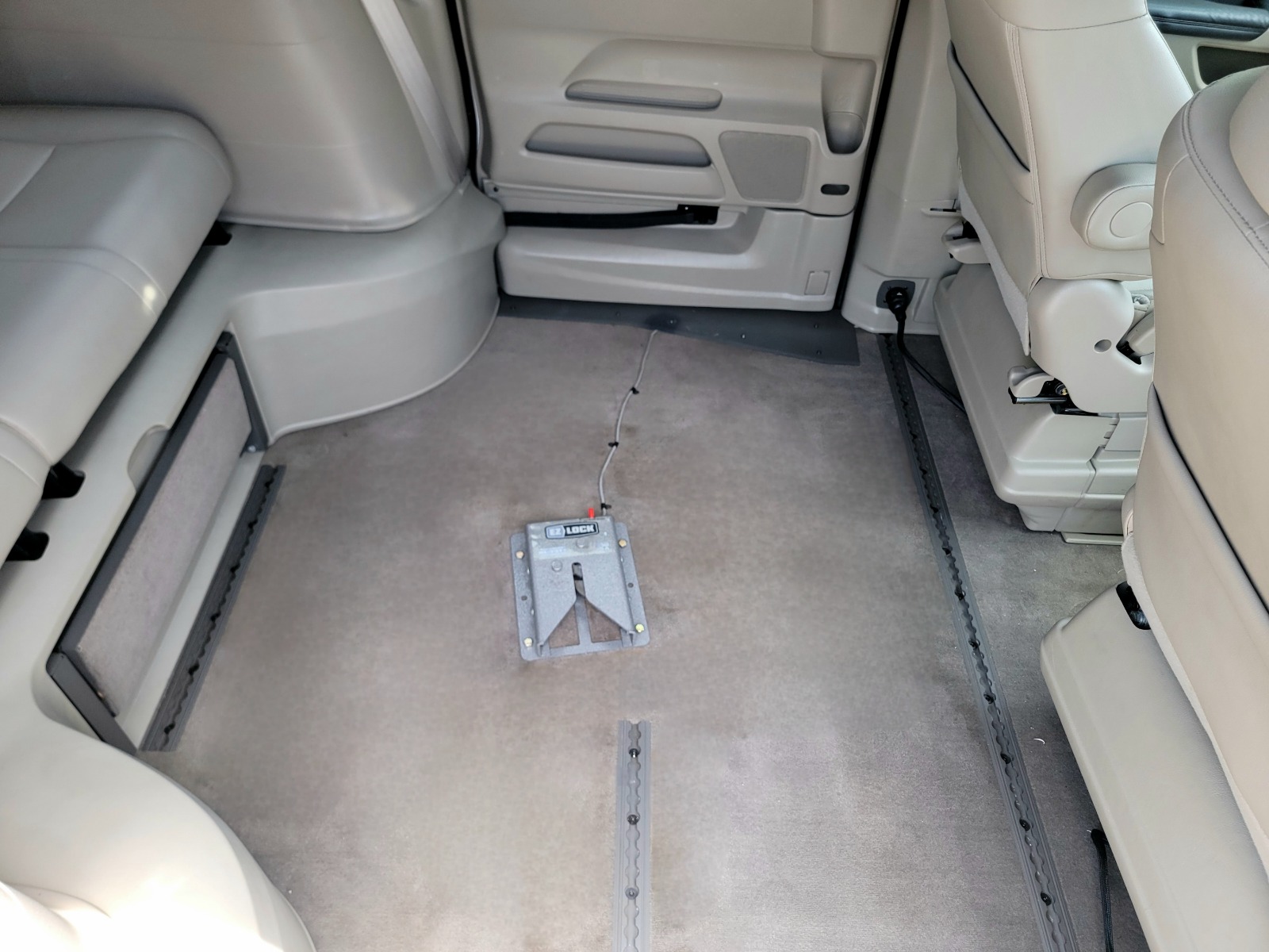 EZ-Lock Dock Installed in Wheelchair Van As seen from the interior of a wheelchair van, a gray square metal dock is bolted down to the middle of the floor ,which is carpeted, in the middle section of a wheelchair van.